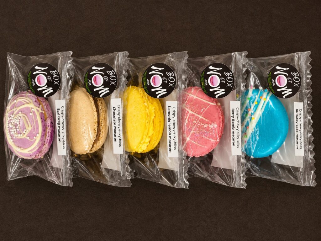 A selection of individually wrapped handcrafted French macarons in assorted flavours, branded by Box of Nom.