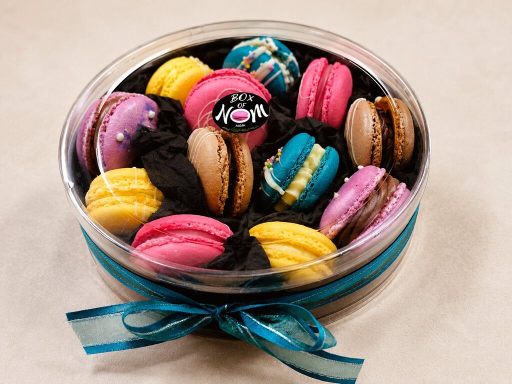 Round gift box filled with handcrafted French macarons, beautifully presented with a teal ribbon by Box of Nom.