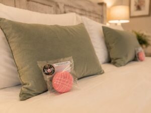 Individually wrapped pink Box of Nom macaron placed on a neatly made bed in a luxury bedroom, creating a thoughtful welcome gift for guests in a Bed and Breakfast