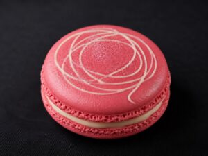 Handcrafted Berry French macaron with vibrant pink shells, creamy berry filling and elegant white chocolate drizzle on a black background.