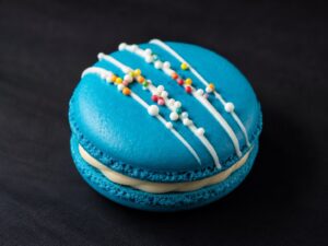 Handcrafted Birthday Cake French macaron with white chocolate drizzle, colourful sprinkles and creamy vanilla filling on a black background.