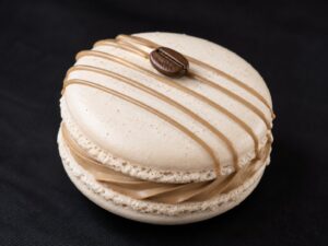 Handcrafted Cappuccino French macaron with creamy coffee filling, caramel drizzle and a coffee bean decoration on a black background.