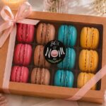 Elegant twelve-piece Box of Nom French macaron gift box featuring handcrafted berry, cappuccino, birthday cake and lemon macarons in premium gift packaging.