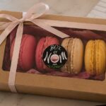 Elegant four-piece Box of Nom French macaron gift box with a pink satin ribbon, featuring handcrafted berry, cappuccino and lemon macarons.