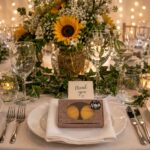 Elegant wedding reception table featuring Box of Nom macaron favour boxes at each place setting, surrounded by sunflower centrepieces, candles and warm fairy lights.
